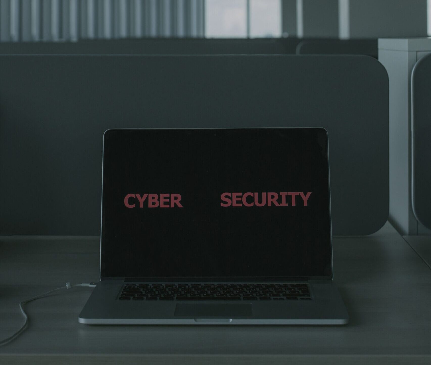 Laptop displaying 'Cyber Security' in a modern office setting, emphasizing tech and cybersecurity themes.